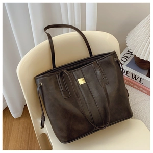 Detail of vintage dark brown leather tote bag with gold buckle on a white chair