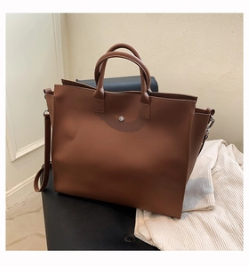 Detailed view of brown tote bag featuring reinforced handles and silver metal hardware