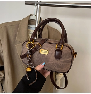 Detail of vintage brown cylinder handbag with golden logo plate and leather handles