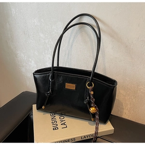 Detail of black faux leather tote bag with gold logo plaque and woven strap charm