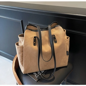 Detail of khaki canvas tote bag with black leather straps and gold rivet accents