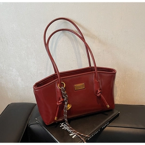 Detail view of burgundy leather tote bag with gold metal plate and woven rope charm