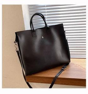 Detail of a large black leather tote bag with round metal buckle on a sunny windowsill