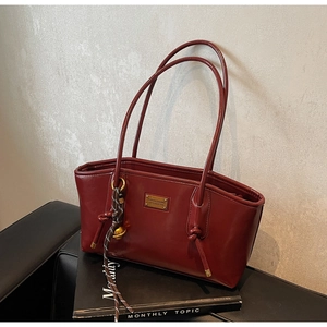 Detail of burgundy faux leather tote bag with gold logo plate and woven bell charm