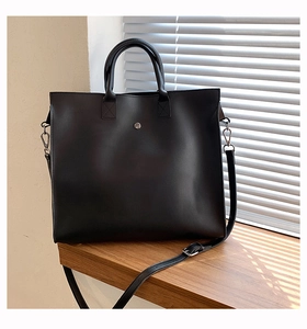 Detail of a black leather tote bag featuring a silver metal buckle and adjustable strap