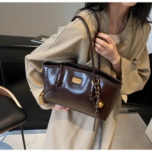 Detail of dark brown glossy PU leather tote bag with gold logo plate and bell charm