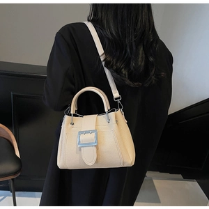 Detail view of cream bucket bag with silver buckle worn on model's shoulder