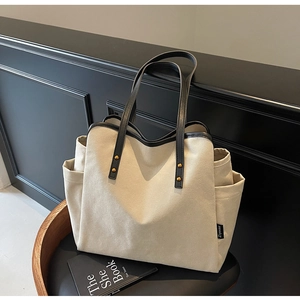 Detail of canvas tote bag showing side pocket, black leather trim and gold rivets