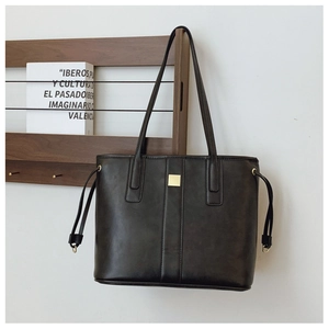 Detail of black leather tote bag with gold buckle and side drawstring on wooden stand