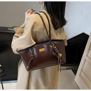 Detail of dark brown oil wax leather tote with gold metal plate and knotted pendant
