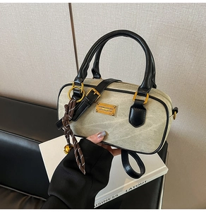 Detail view of a green Boston handbag featuring black leather trim and golden logo plate