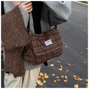 Brown plaid crossbody bag with fabric label and black strap worn over a grey hoodie
