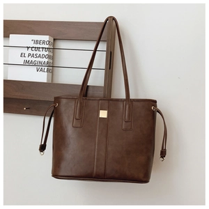 Detail of dark brown leather tote featuring gold metal square and side drawstring accents