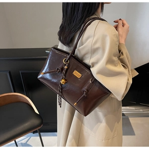 Detail of dark brown wax leather tote bag with gold metal pendant and drawstring