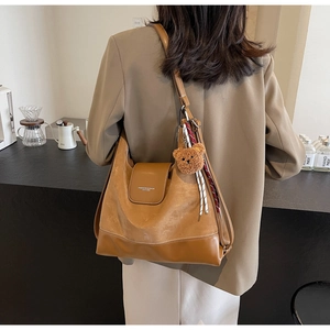 Brown leather tote bag detail with adjustable strap, bear charm and silk scarf accent