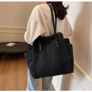 Close-up of black canvas tote bag showing outer pocket and faux leather handles