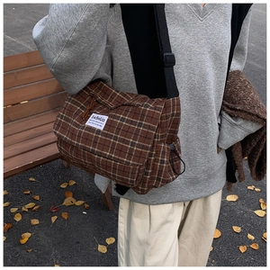 Close-up of brown plaid crossbody bag with nylon strap and woven label detail