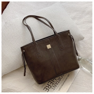 Detail of a dark brown vintage tote bag with gold metal plaque and drawstring accents