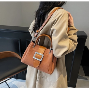 Caramel brown bucket bag with large silver buckle shown on shoulder of a trench coat