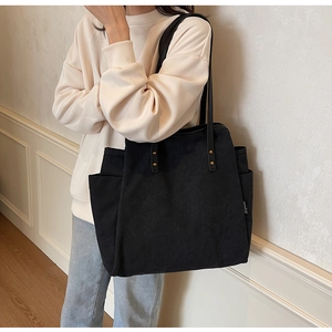 Detail of black canvas tote bag showing side pockets and gold rivet reinforcements