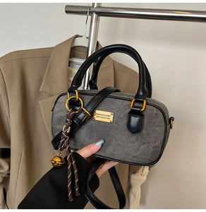 Detail of grey fabric bag with black leather trim, gold hardware and bell charm