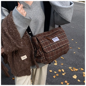 Detail view of brown plaid canvas crossbody bag with black adjustable strap on shoulder