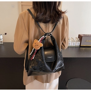Close-up of black leather backpack with brown bear charm and white stitching detail