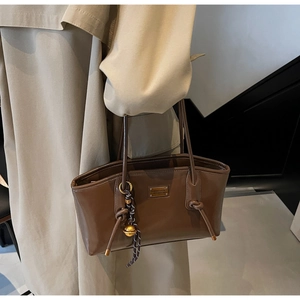 Detail of a brown leather tote bag with gold hardware and woven pendant on khaki coat