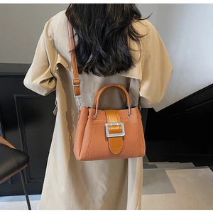 Detail of orange-brown woven bucket bag with silver buckle worn with beige coat