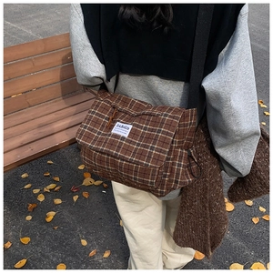 Detailed view of brown checkered messenger bag with logo patch in an autumn setting