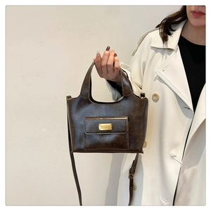 Gros plan d'un sac seau vintage en cuir marron porté par un mannequin en trench beige