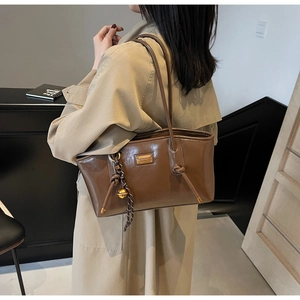 Detail of dark brown leather tote bag featuring golden logo plate and knot decoration