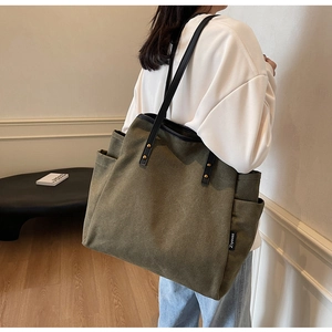 Detail of olive green canvas tote bag with black leather straps and gold rivets