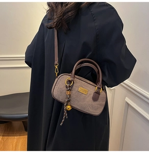 Detail of dark taupe textured handbag with golden metal plate and decorative bell charm