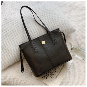 Detail of dark brown leather tote bag with gold buckle and drawstring on white cushion