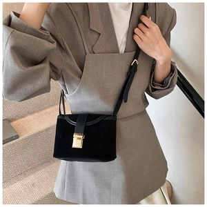Detail of a vintage black matte crossbody bag with a gold buckle worn by a model
