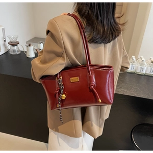 Detail of burgundy glossy leather tote bag with gold nameplate and tassel charm