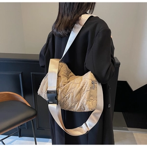 Detail of beige quilted crossbody bag featuring wide nylon strap and buckle on model