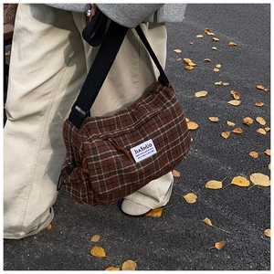 Close-up of brown checkered underarm bag with adjustable strap and brand patch