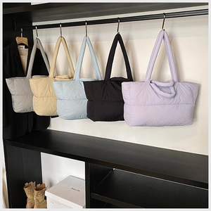 Quilted puffer tote bags in grey, beige, blue, black and purple hanging on a rack