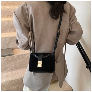 Detail of black suede crossbody bag with vintage golden buckle on a beige backdrop