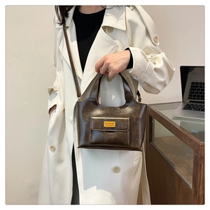Gros plan d'un sac seau vintage en cuir marron avec plaque logo en métal et poche frontale