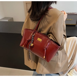Detail of burgundy glossy leather shoulder bag with gold hardware and striped ribbon