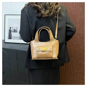 Sac seau vintage marron en similicuir avec plaque dorée porté sur un tailleur noir
