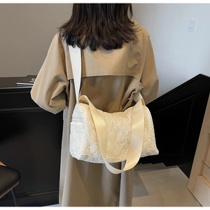 Detailed embroidery of white quilted floral crossbody bag on a beige trench coat