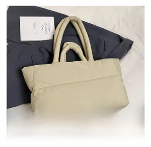 Detail of beige quilted puffer tote bag on grey suit and book for commute
