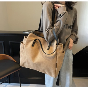 Close-up of khaki canvas tote bag featuring black leather straps and side pocket detail