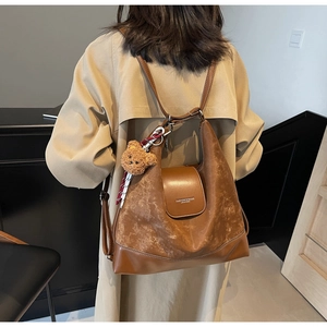 Detail of vintage brown leather tote bag with teddy bear charm on beige trench coat