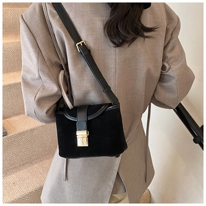 Detail of a black matte crossbody bucket bag with gold hardware on a model