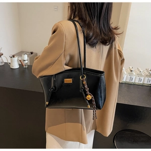 Detail of a black leather tote bag featuring a gold nameplate and braided pendant detail